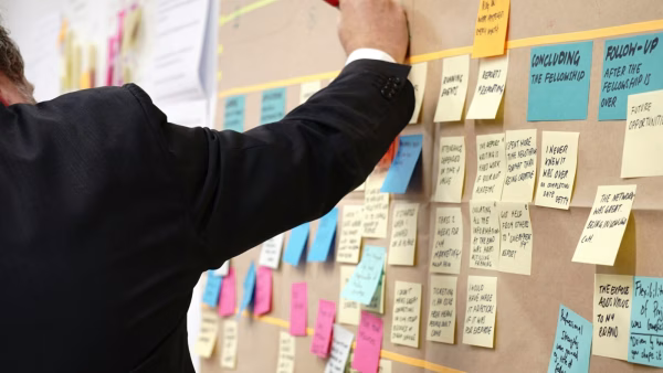 Person writing on colorful sticky notes on a whiteboard during a planning session